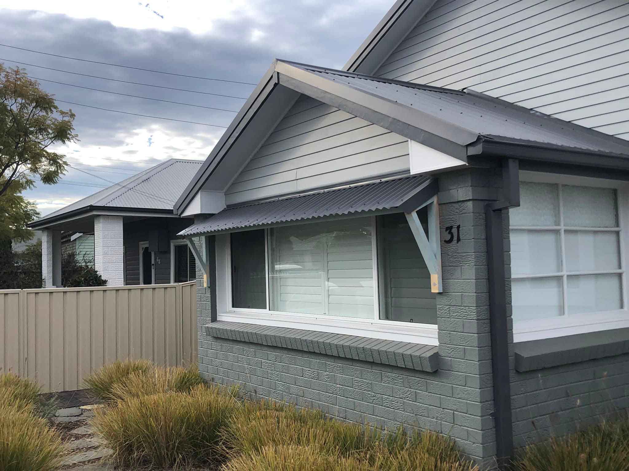 Front of a grey brick and weatherboard house with a window awning