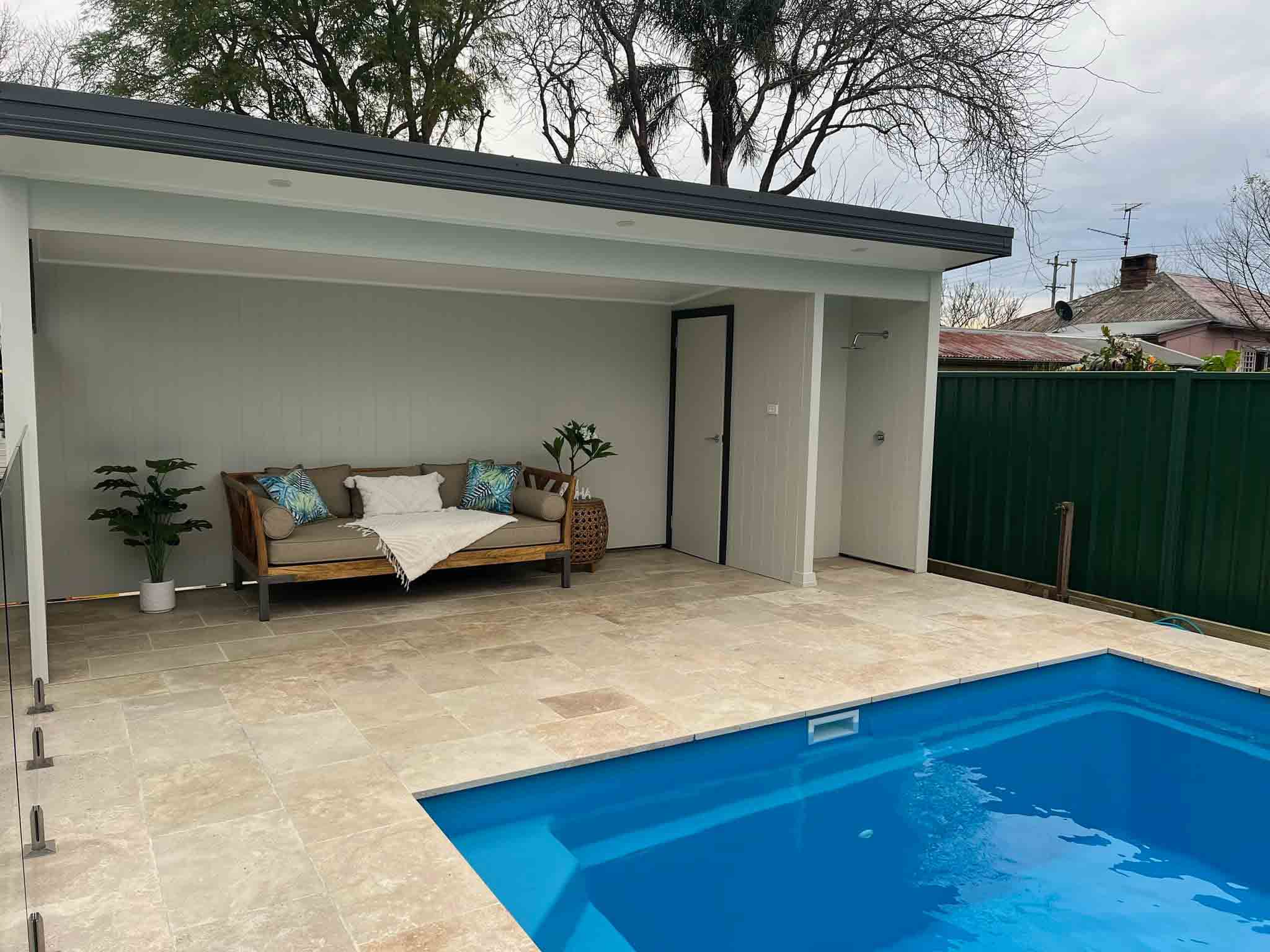 Covered outdoor room with a daybed beside an in-ground pool