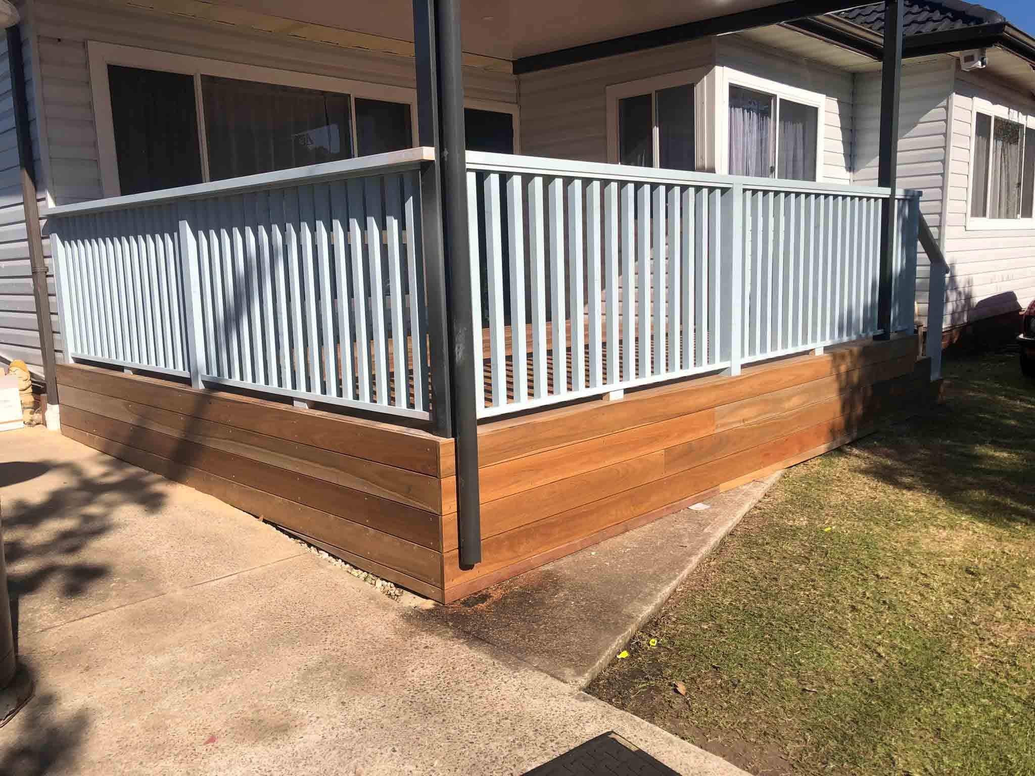Raised timber deck with white balustrade beside a weatherboard house