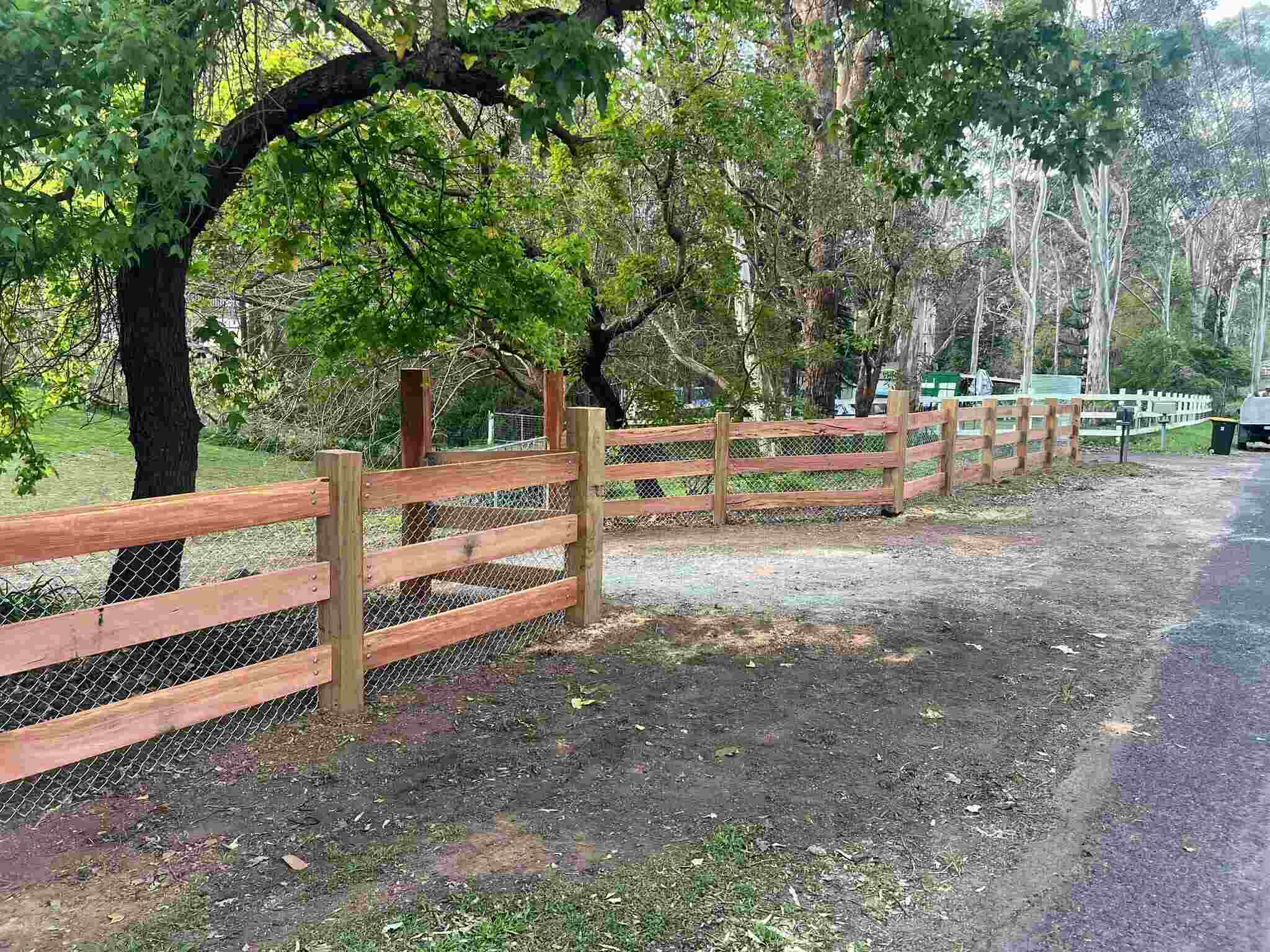 Timber post-and-rail fence with wire mesh beside a gravel road