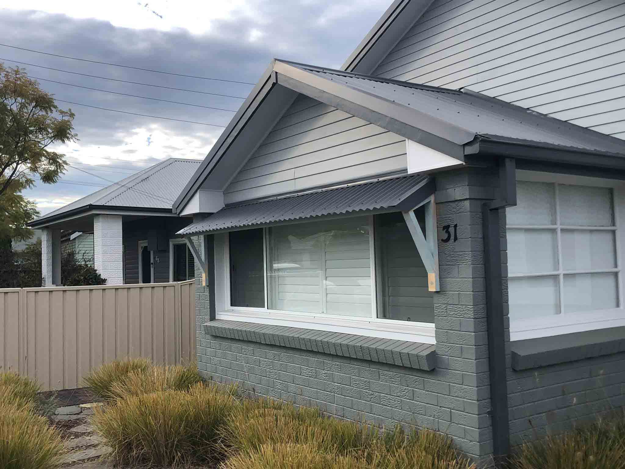 Grey brick and weatherboard house front with a window awning and garden