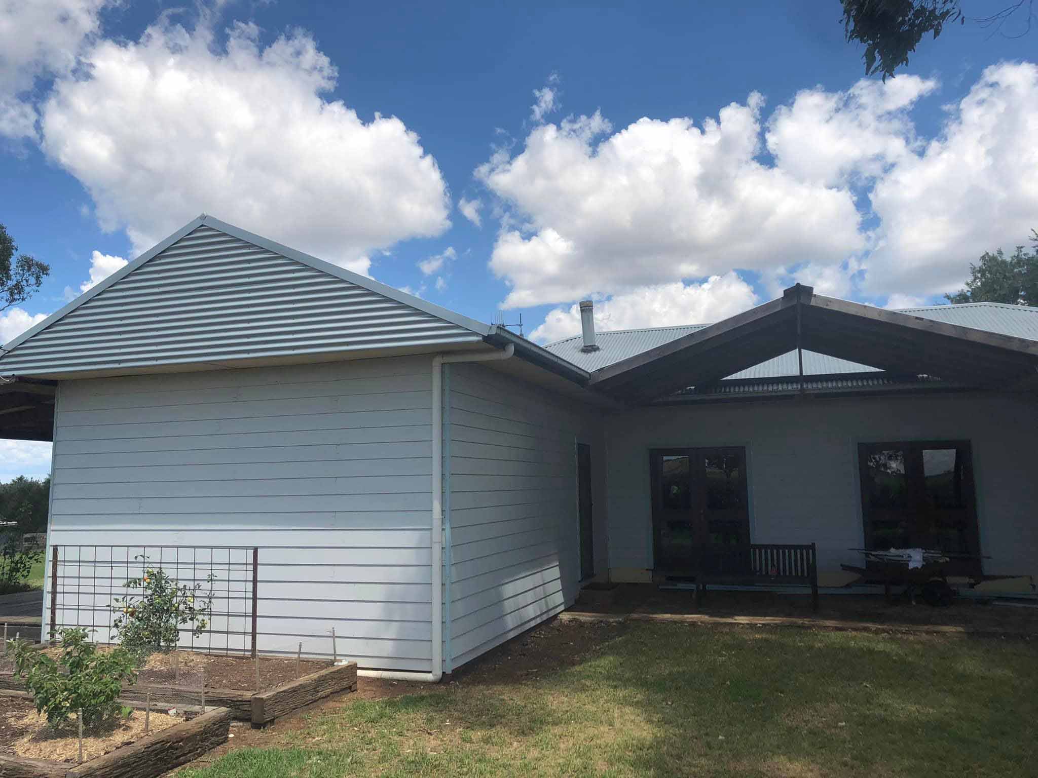 Weatherboard extension with a gabled roof beside raised garden beds