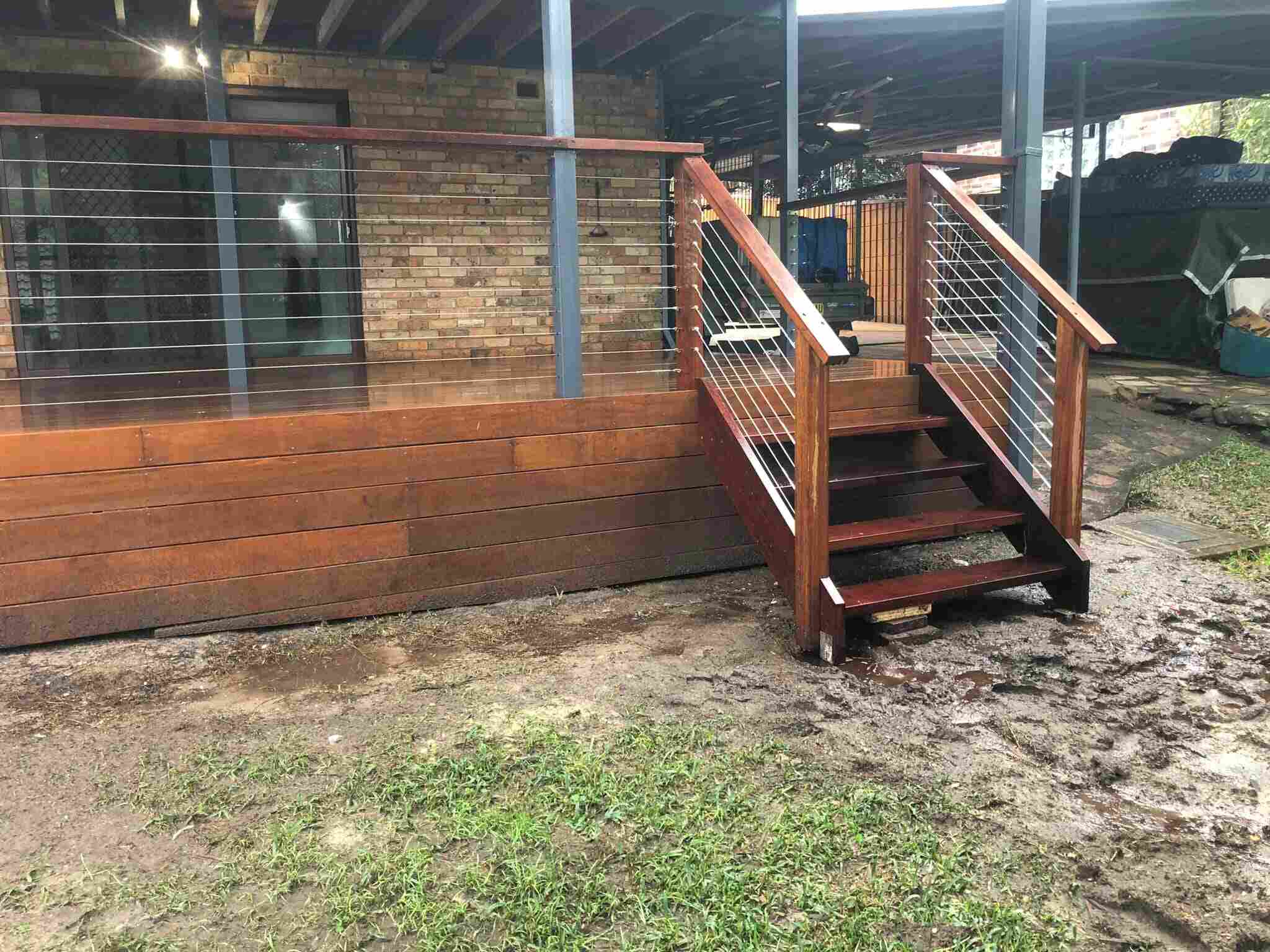 Timber deck with wire balustrade and side stairs beside a brick house