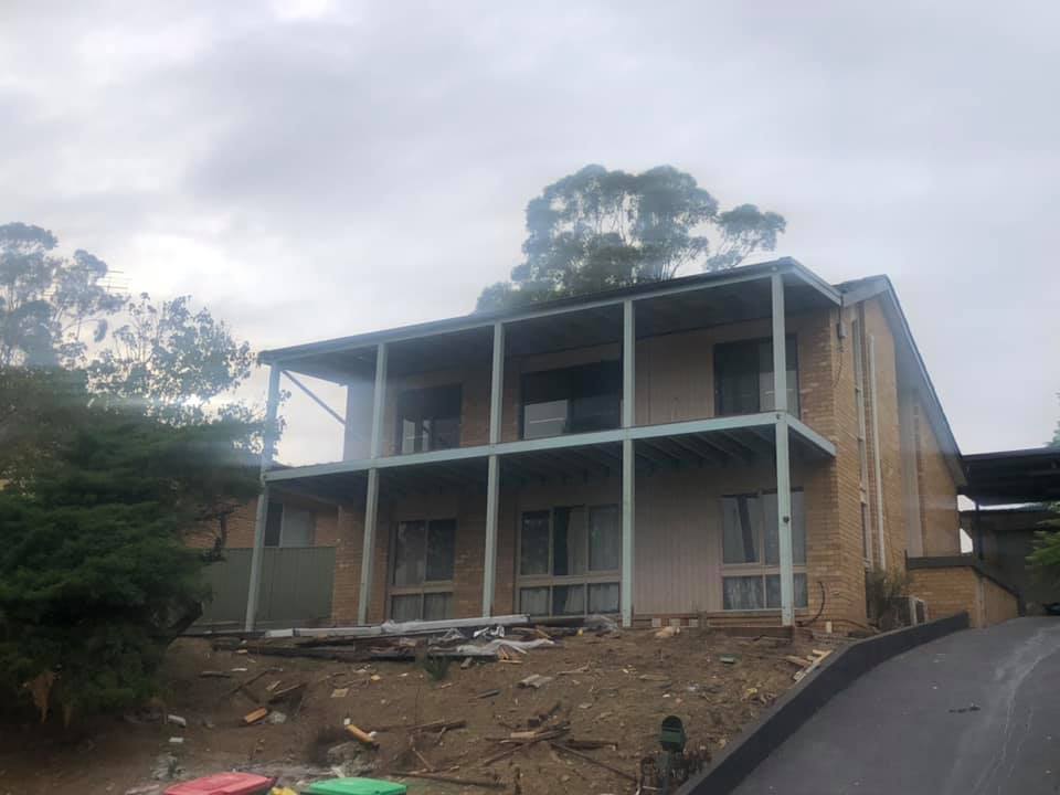 Two-storey brick house with upper and lower verandahs, building rubble in front