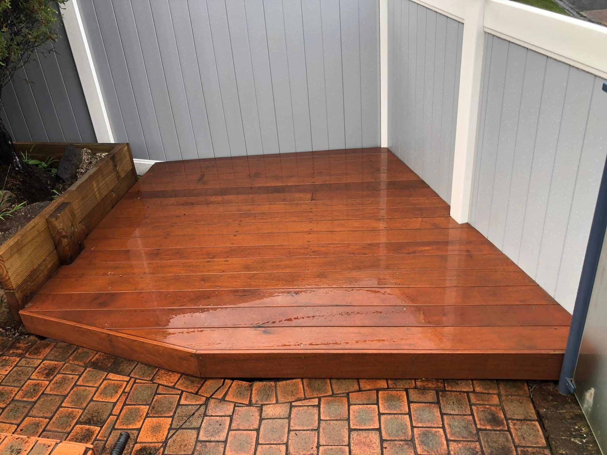 Glossy timber deck fitted into a fenced corner on brick paving
