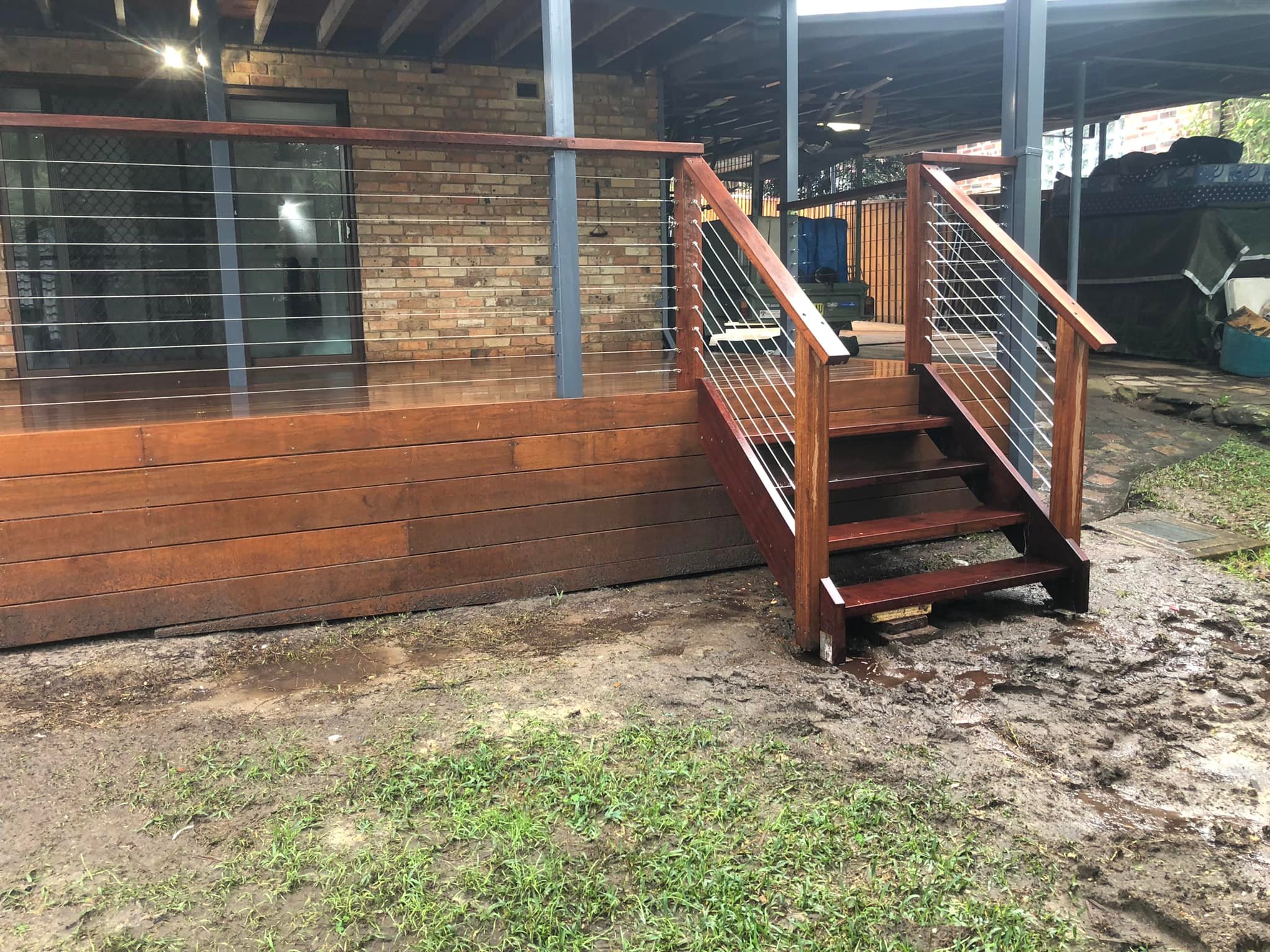 Timber deck with wire balustrade and stairs beside a brick house