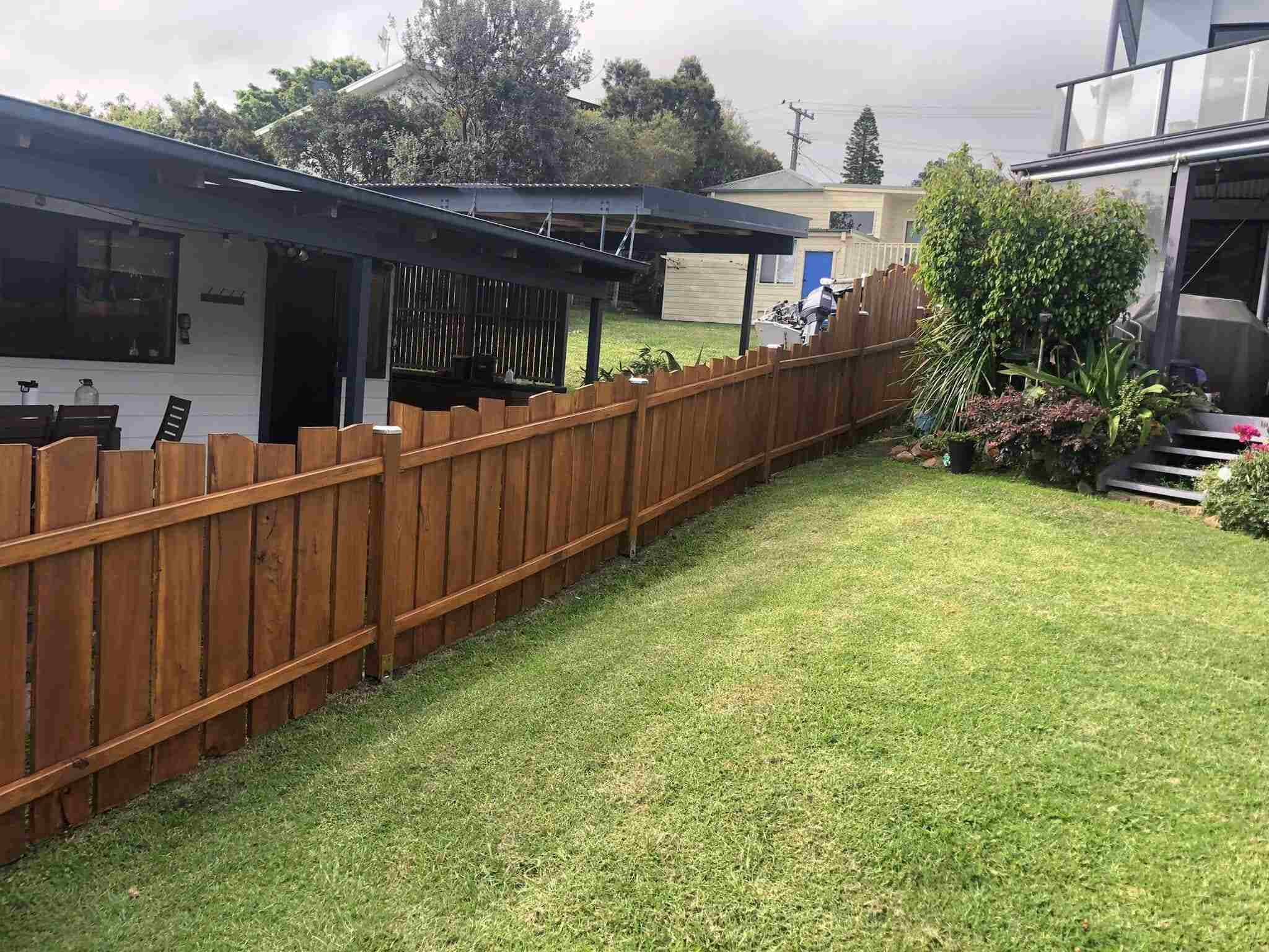 Stained timber paling fence beside a sloping lawn and covered patio