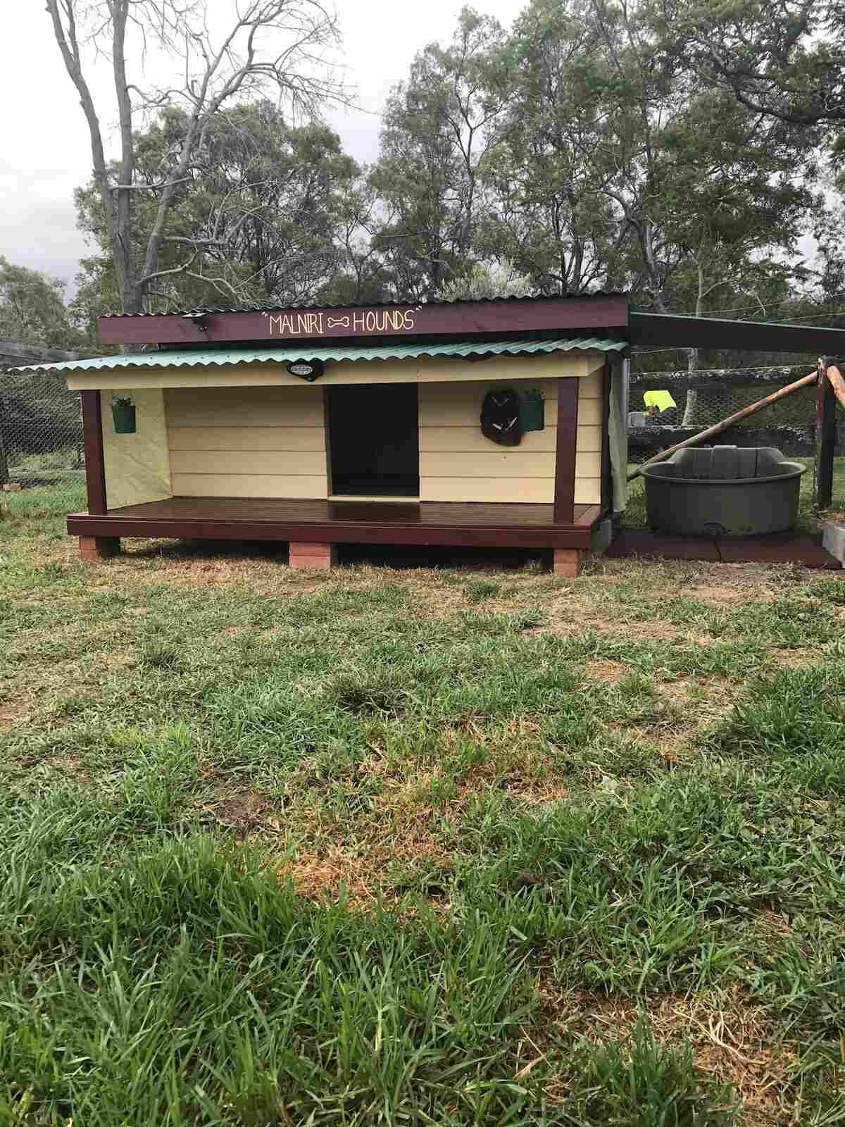 Dog kennel with a timber deck on a grassy block, seen from a distance