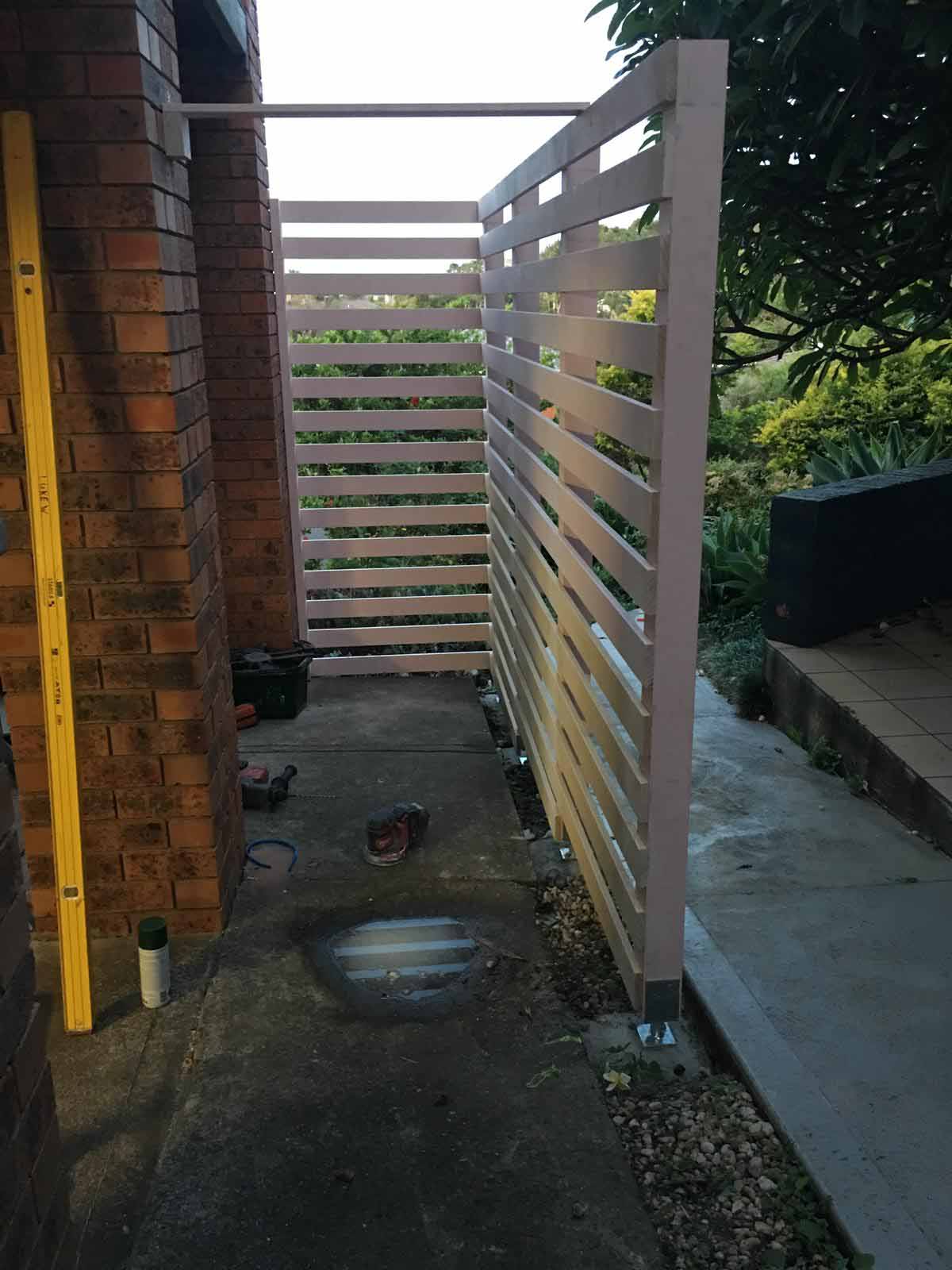 Slatted screen being installed along a brick side passage